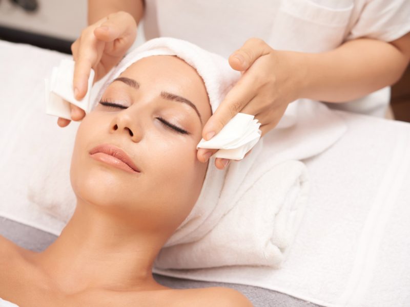 Beautician taking off excess of serum from face of client at the end of spa procedure